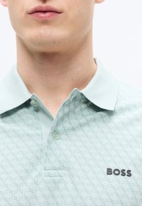 Ανοιχτό πράσινο πόλο μπλουζάκι μέντας με υφασμένο εξαγωνικό σχέδιο, δύο κουμπιά κοντά στο γιακά και μαύρο λογότυπο "BOSS" στο στήθος.