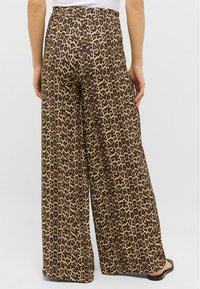 Hlače širokih nogavica s uzorkom leopard, visoki struk, glatke teksture, s bež pozadinom i tamnosmešnim mrljama.