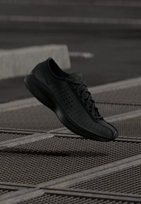 Pantofii sport negri au un design minimalist, cu un superior perforat și vârf rotund. Acestia sunt echipați cu șireturi plate și o talpă căptușită pentru confort.
