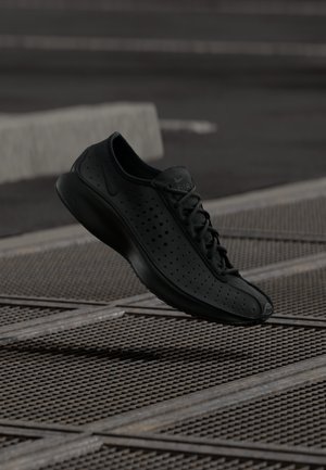 Zwarte sportschoen met geperforeerde bovenkant, ronde neus en minimalistisch ontwerp. Voorzien van platte veters en een gevoerde zool voor comfort.