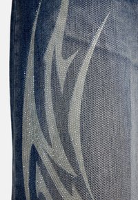 Ύφασμα τζιν σε σκούρο μπλε χρώμα με λαμπερό, ανοιχτό γκρι φυλετικό σχέδιο. Λεπτό υφή με εμφανείς κλωστές ύφανσης και διακριτική λάμψη.