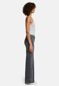 Jeans gris évasés à taille haute, avec une fermeture à bouton et fermeture éclair à l'avant, et un tissu texturé. Associés à un débardeur gris clair.