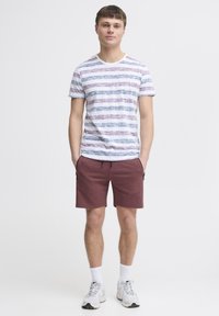 T-shirt rayée en blanc, bleu et bordeaux avec un col rond associé à un short bordeaux. Des chaussures de sport décontractées et des chaussettes blanches complètent le look.