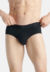 Culottes en coton noir avec une large ceinture élastique, présentant un logo subtil. Le design est ajusté avec une texture douce et un aspect sans couture.