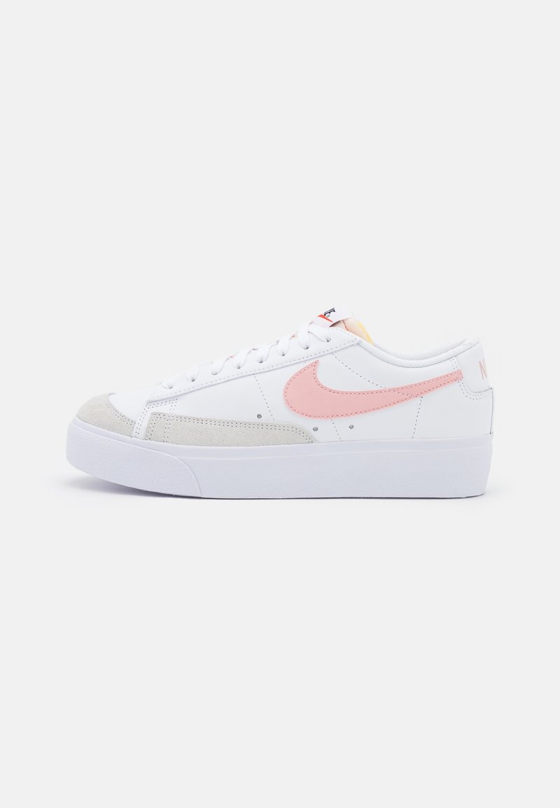 Zapatilla blanca con puntera de ante gris, el swoosh de Nike en rosa y cordones blancos. Cuenta con una suela texturizada y un logo sutil en el talón.