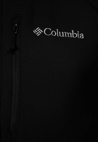 Czarna polarowa kurtka z zamkiem błyskawicznym w kieszeni na piersi, z białym wyszywanym logo w lewym górnym rogu. Gładka faktura.