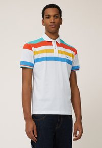 Witte polo met kleurrijke horizontale strepen in rood, oranje, geel, blauw en turquoise. Voorzien van een kraag en een knoopsluiting met twee knopen.