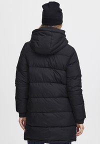 Svart dunjakke med hette, vertikal quiltet mønster, elastiske mansjetter og en middels lang lengde. Materialet ser glatt og isolert ut.