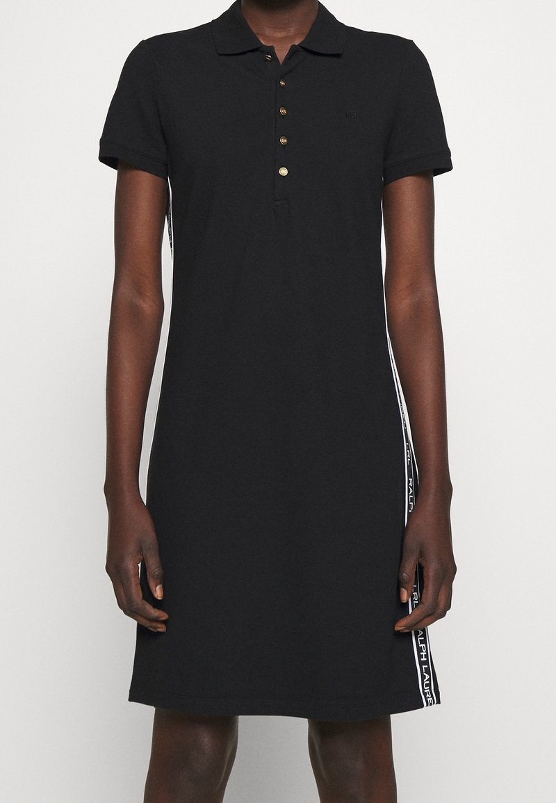 Svart polo-klänning i bomull, med korta ärmar, krage, fem guldknappar och vita sidostreck med textaccenter.