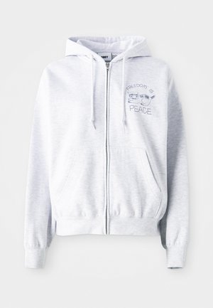 Svijetlo siva zip-up dukserica s kenguru džepom. Ima izvezeni tekst: "SLOBODA JE" iznad mačke i "MIROVANJE" ispod. Mekana tkanina od pamučne mješavine.