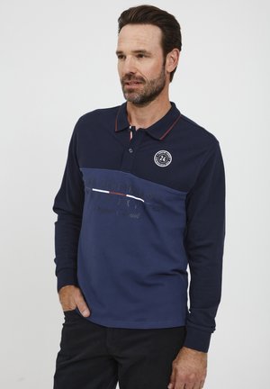 Marineblå langærmet polo-shirt med tofarvet design, røde krave accenter, logo på forsiden og grafisk tekst. Lavet af bomuldsmateriale med en blød tekstur.
