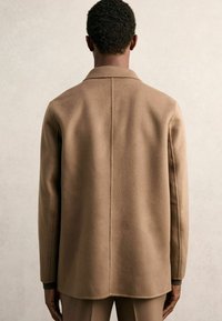 Braune Wollmischungjacke mit Reverskragen, taillierter Passform und glatter Textur. Hat eine gerade Rückennaht und Seitentaschen.