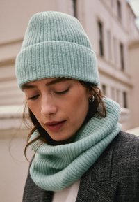 Light blue knit beanie and matching cowl scarf, featuring ribbed texture. Both accessories are made from soft, warm material.