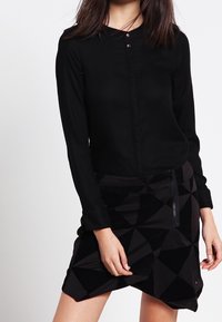 Black long-sleeve blouse with round neckline and two buttons, paired with a geometric-patterned black skirt featuring a side zipper.