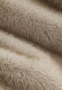 Gestructureerde imitatiebont in zachte beige tinten, met fijne draadjes en een weelderig uiterlijk, wat een warme en gezellige oppervlakte creëert.