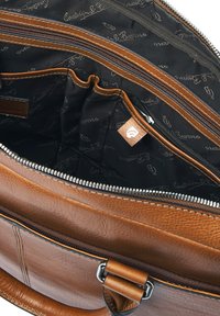Bolso de cuero marrón abierto para mostrar el interior de tela negra con múltiples bolsillos con cremallera y bolsillos deslizables, costuras blancas y forro de marca.