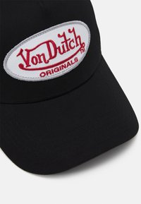 Zwarte pet met een ovale witte patch met "Von Dutch" in rode geborduurde letters en "ORIGINALS" eronder in een kleinere lettergrootte.
