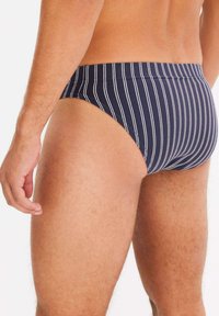 Pantaloni da bagno a righe navy con una texture liscia, caratterizzati da righe verticali bianche e un taglio aderente. Vita elasticizzata senza hardware aggiuntivo.