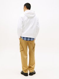 White hooded sweatshirt with a kangaroo pocket, worn over a blue plaid shirt. Tan cargo pants with side pockets and black shoes.