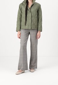 Olivgrön vadderad jacka med tryckknappar och två frampocket, kombinerad med rutiga utsvängda byxor och ljusbeige ballerinas.