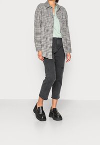 Giacca a pulsante a quadri grigia e nera, blusa verde chiaro, pantaloni cropped in denim neri e scarpe slip-on in platform nere.