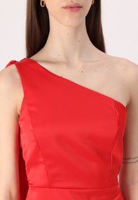 Robe en satin rouge avec un design asymétrique à une épaule. Texture lisse avec un détail de nœud discret à l'épaule.