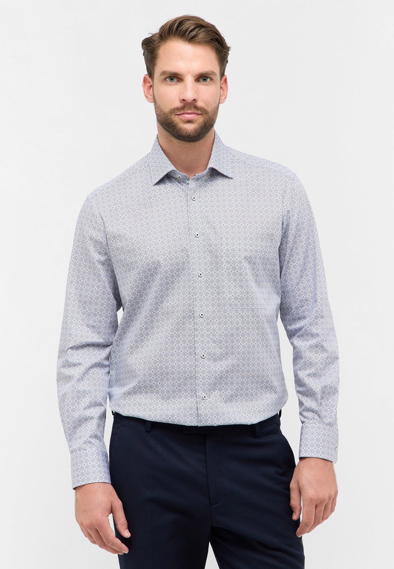 Camicia azzurro chiaro con un motivo geometrico, colletto button-down e maniche lunghe, abbinata a pantaloni scuri. Tessuto dalla consistenza liscia.