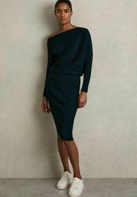 Pletené tmavozelené šaty s off-shoulder strihom, priliehavým strihom, ryhovanou textúrou a kombinované s bielymi teniskami.