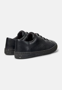 Sneakers in pelle nera con una finitura texture, punta rotonda, suola piatta nera con macchie bianche e lacci neri. Nome del marchio visibile sulla suola.