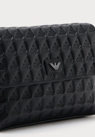 Μαύρο δερμάτινο τσαντάκι χειρός με υφή γεωμετρικού μοτίβου και μικρό ασημένιο έμβλημα στην μπροστινή πτέρυγα.