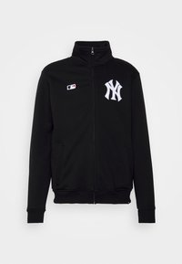Sort zip-jakke lavet af blødt stof, med høj krave, to sidelommer og hvidt broderet New York Yankees-logo på brystet.