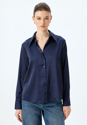 Granatowa satynowa bluzka z klasycznym kołnierzykiem, długimi rękawami i zapięciem na guziki z dopasowanymi guzikami. Gładka tekstura i luźny krój.
