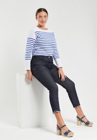 Blauwe en witte gestreepte longsleeve shirt, donkerdenim jeans en marineblauwe platform schoenen met houten hak. Gladde texturen, opgerolde mouwen van de jeans.