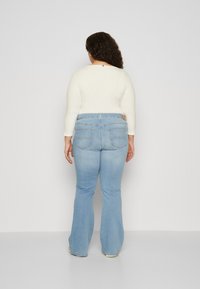 Helle blau ausgestellte Jeans mit mittelhohem Bund, kombiniert mit einem cremefarbenen Strickoberteil mit Dreiviertelärmeln. Die Rückansicht zeigt Detailnähte.