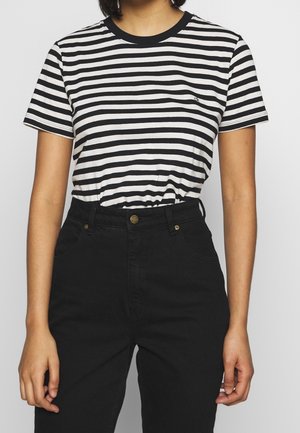 Femme portant un t-shirt à manches courtes rayé horizontalement noir et blanc, rentré dans un pantalon noir taille haute.