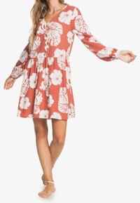Czerwona sukienka w kwiaty z długimi rękawami, zdobiona białymi wzorami hibiskusa i liści, z dekoltem w serek i guzikami z przodu. Luźny krój.