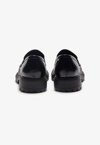 Pantofi din piele neagră cu un design elegant, margini rotunjite și o talpă groasă din cauciuc, având un model texturat de profil.