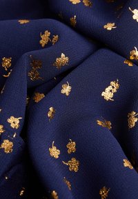 Marinblått tyg med en texturerad yta, som har guldiga blommönster genom hela. Materialet är mjukt och faller elegant.