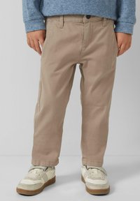 Beżowe bawełniane spodnie o prostym kroju, z przednimi kieszeniami i zapięciem na guzik, w połączeniu z białymi i szarymi trampkami; materiał o fakturze.