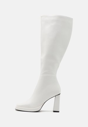 Stivale bianco fino al ginocchio realizzato in materiale liscio, con tacco alto spesso e punta leggermente quadrata con dettagli neri sulla suola.
