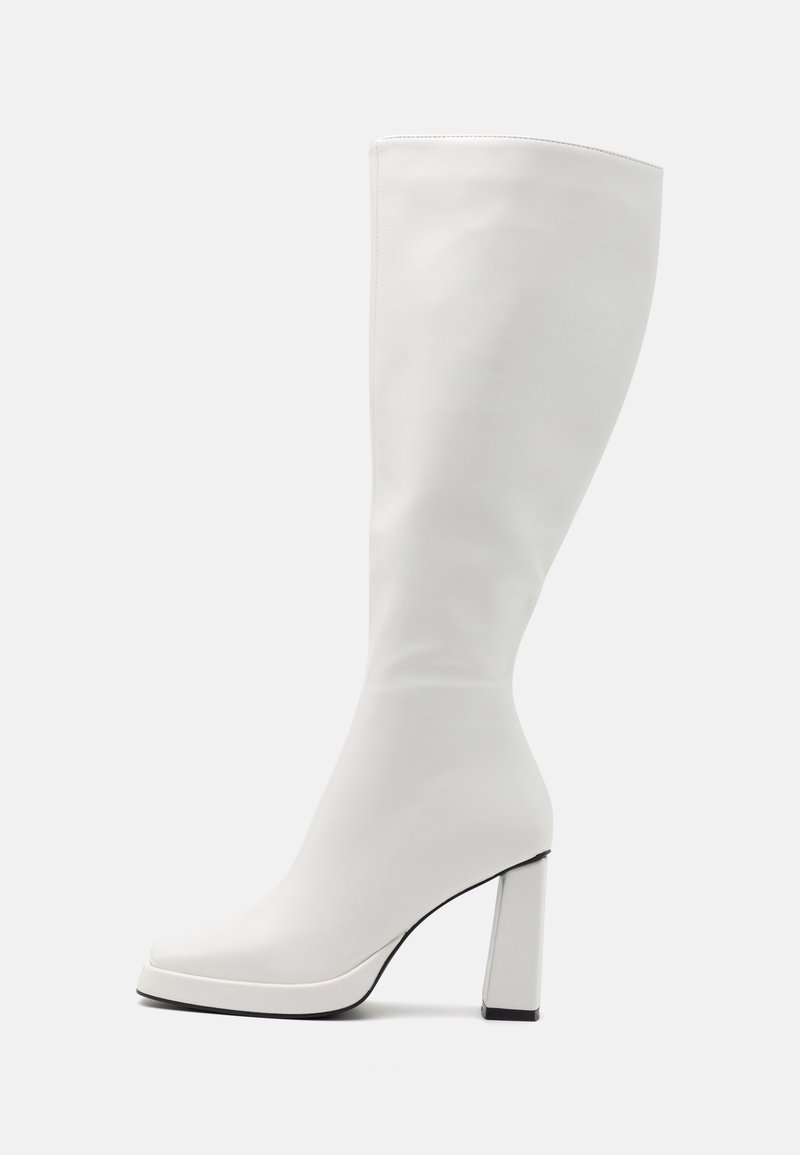Botte blanche jusqu'au genou en matériau lisse, dotée d'un talon haut épais et d'un embout légèrement carré avec des accents noirs sur la semelle.