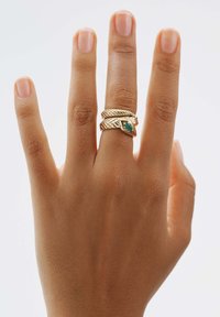Conjunto de anillos apilados de oro con un diseño de serpiente, que presenta un acento de piedra preciosa verde suave. Mostrado en un dedo sobre un fondo neutro.