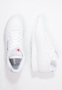 White athletic shoes with a smooth leather finish, perforated toe, and textured accents. Features contrasting logo and laces in a classic design.