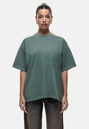 Groene oversized T-shirt van zachte stof, met een ronde hals, verlaagde schouders en contrasterende naden. Gepaarde met donkere broeken.