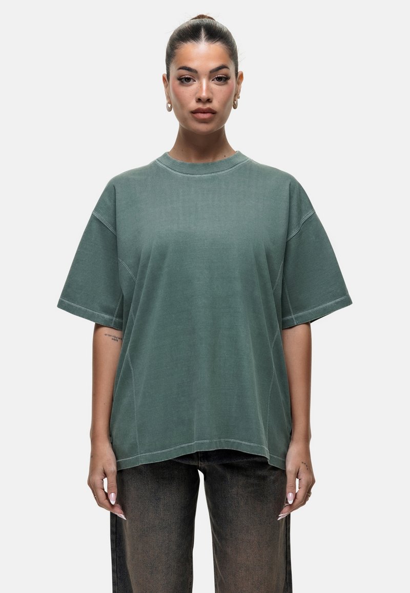 Zielony, oversize T-shirt z miękkiego materiału, z okrągłym dekoltem, opuszczonymi ramionami i kontrastowymi detalami szwów. W połączeniu z ciemnymi spodniami.