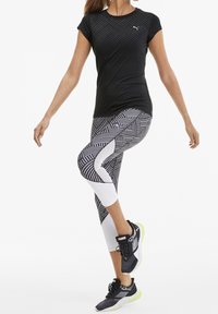 Svart kortärmad träningstopp med geometrisk textur; leggings med svart- och vitt mönster och vit panel; svarta sneakers med gröna detaljer.