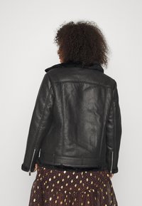 Giacca in pelle nera con una finitura testurizzata, colletto foderato in pelliccia e cerniere sui polsini. Indossata sopra una gonna a strati con motivo.