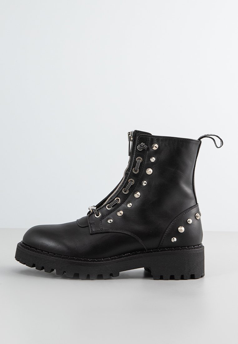 Bottine en cuir noir ornée de clous en métal argenté, avec une fermeture éclair sur le côté et une semelle en caoutchouc épaisse à motif texturé.