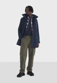 Mornarski vodootporni jakna preko karirane košulje i mornarsko plave majice, uparen s zelenim cargo hlačama i crnim tenisicama. Ima patentne zatvarače i džepove.