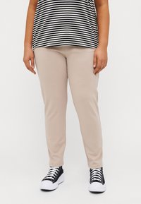 Beige fitted pants made of stretch fabric, featuring a smooth texture. Paired with black and white sneakers. Vertical stripes on the top.
